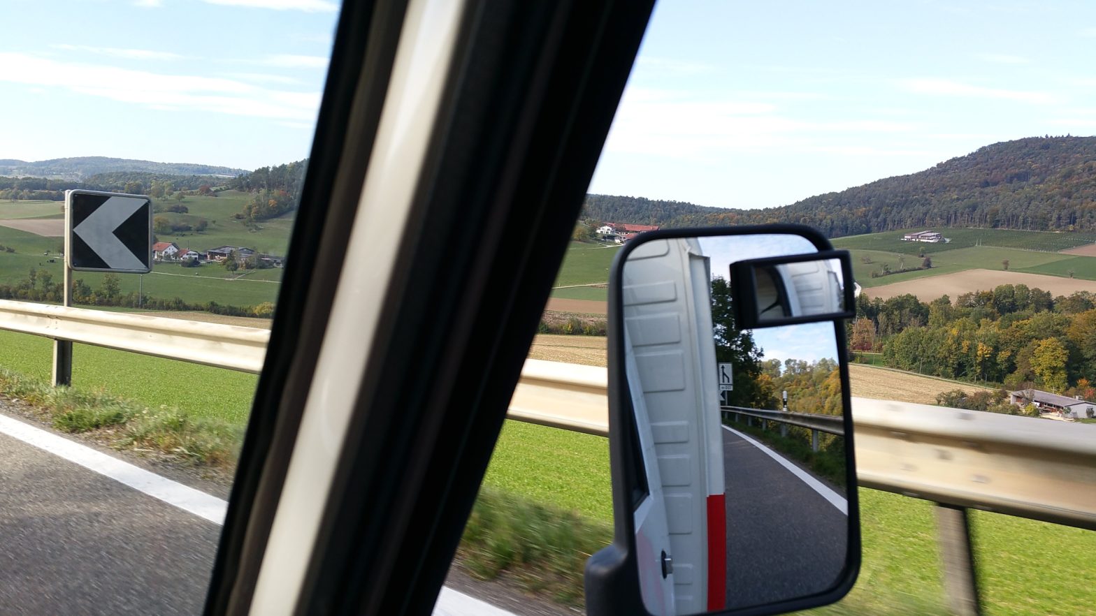 Landschaft Schweiz aus Fahrzeug zentral der Rückspiegel in dem sich ein Schild spiegelt